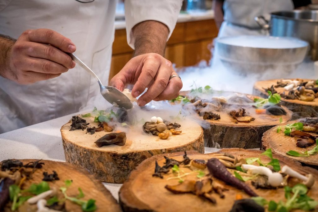 Restauration raffinée A chef artfully plating a gourmet dish with mushrooms and greens on wood slices.